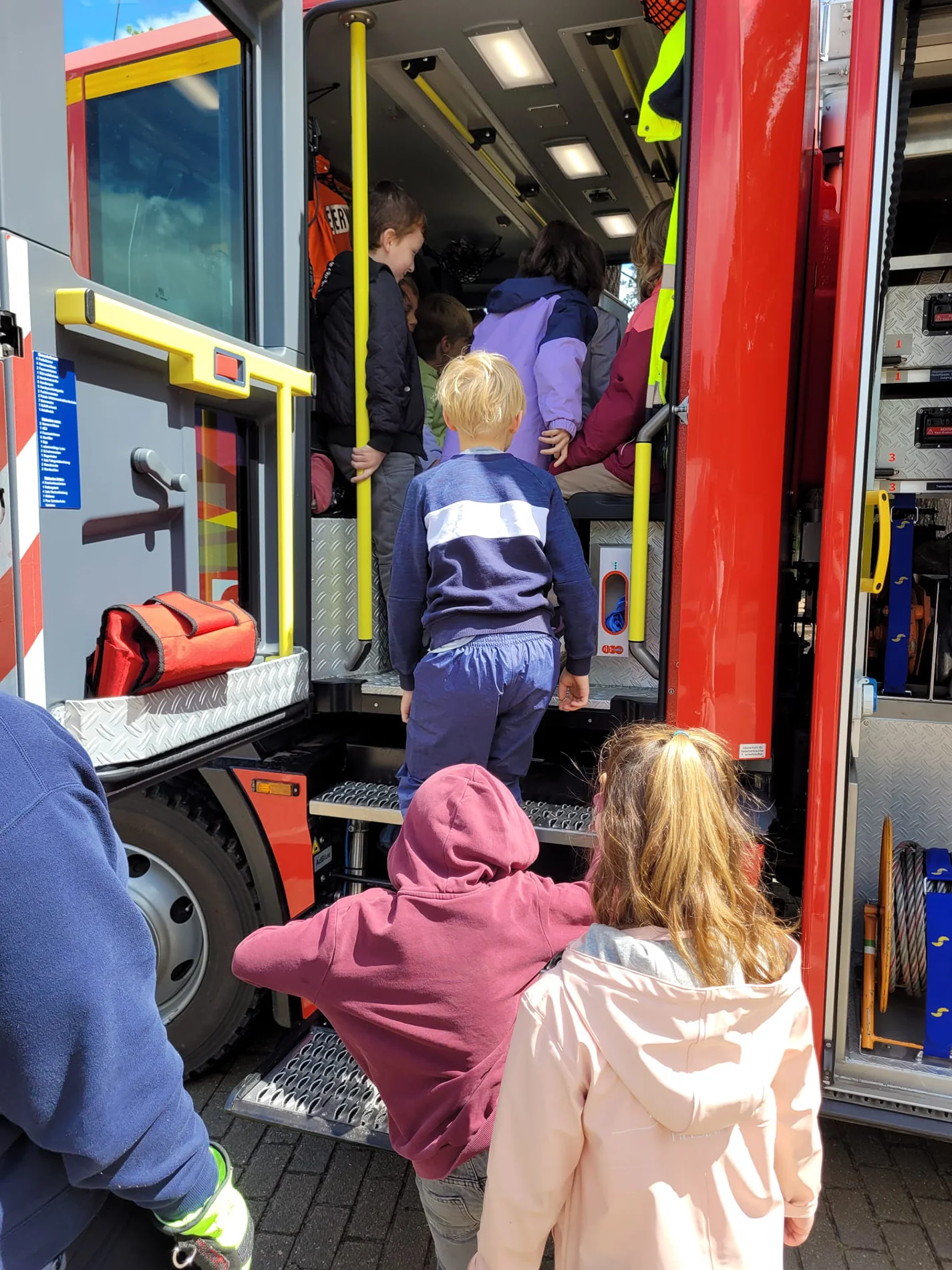 Kinder steigen in ein Feuerwehrauto ein und erkunden den Innenraum.