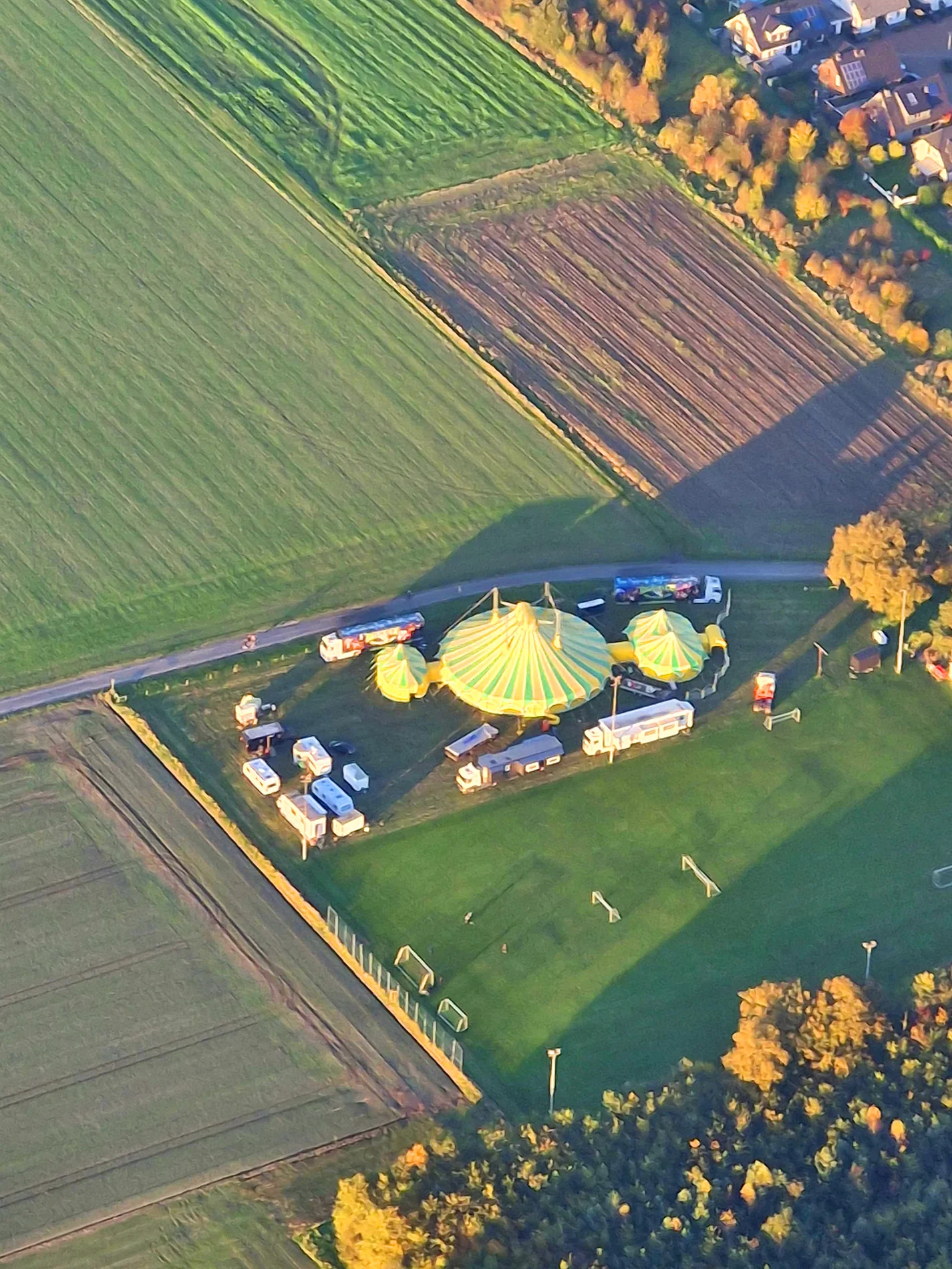 Luftaufnahme eines großen gelb-grünen Zirkuszelts mit umliegenden Wagen und Feldern.