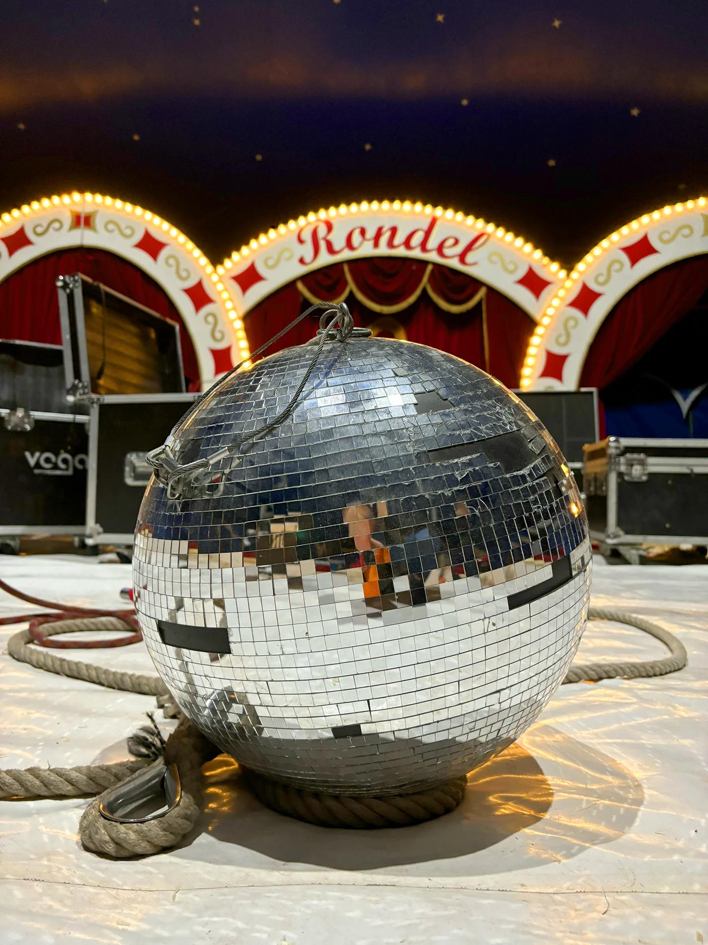 Discokugel liegt auf dem Boden einer Manege, im Hintergrund die beleuchtete Zirkusdekoration.