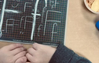 Kind übt auf Schreibtafel das Schreiben des Buchstabens F mit Kreide – erste Schreibübungen im Unterricht.