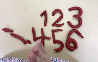 Kind formt Zahlen und Buchstaben aus Knete – spielerisches Lernen im Anfangsunterricht.