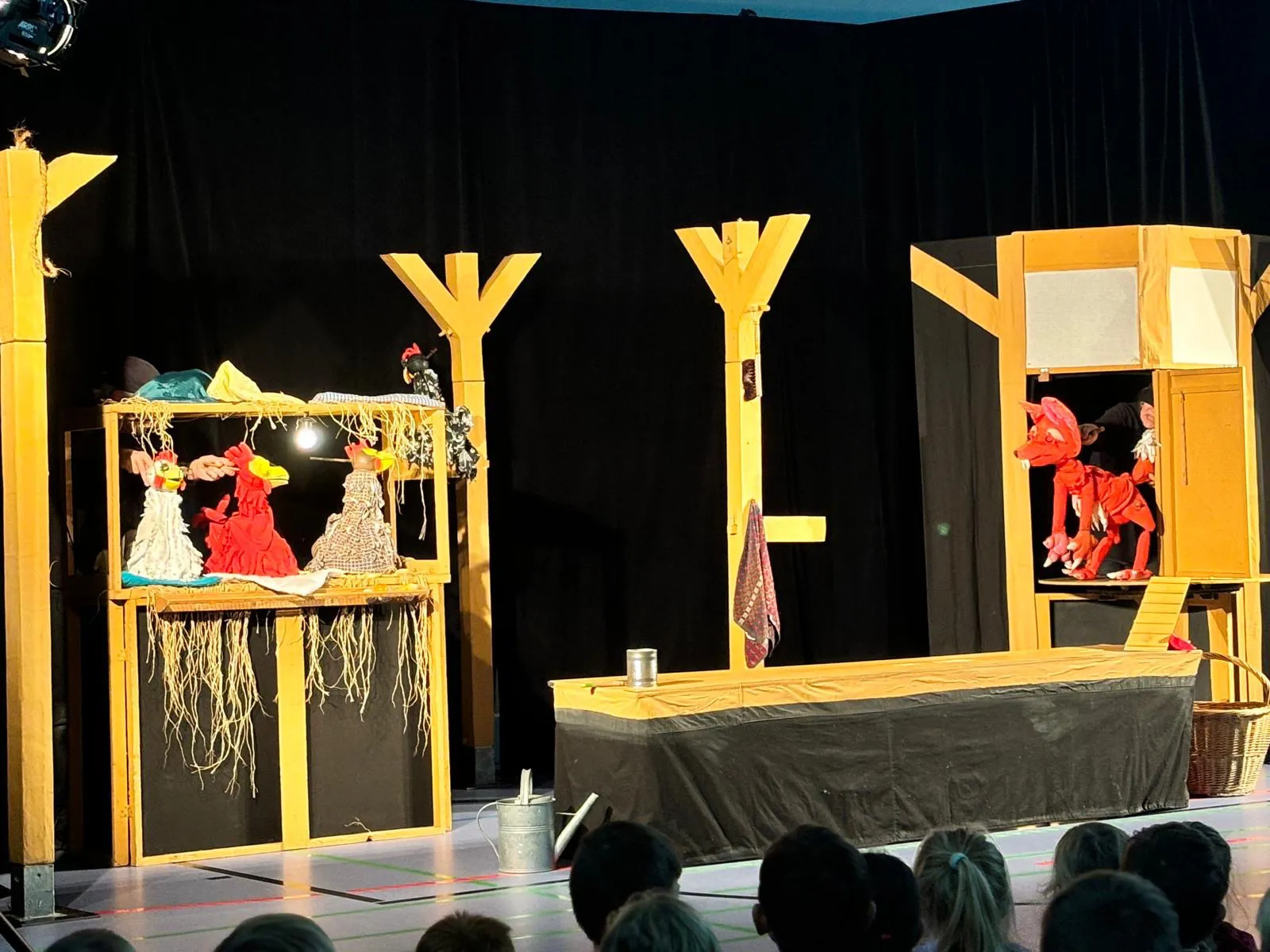 Figurentheater-Aufführung mit bunten Handpuppen auf einer Schulbühne, vor einem Publikum aus Kindern