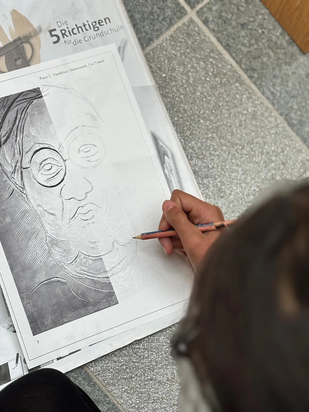 Ein Kind zeichnet ein Porträt von Otto Pankok nach, Vorlage liegt auf dem Boden.