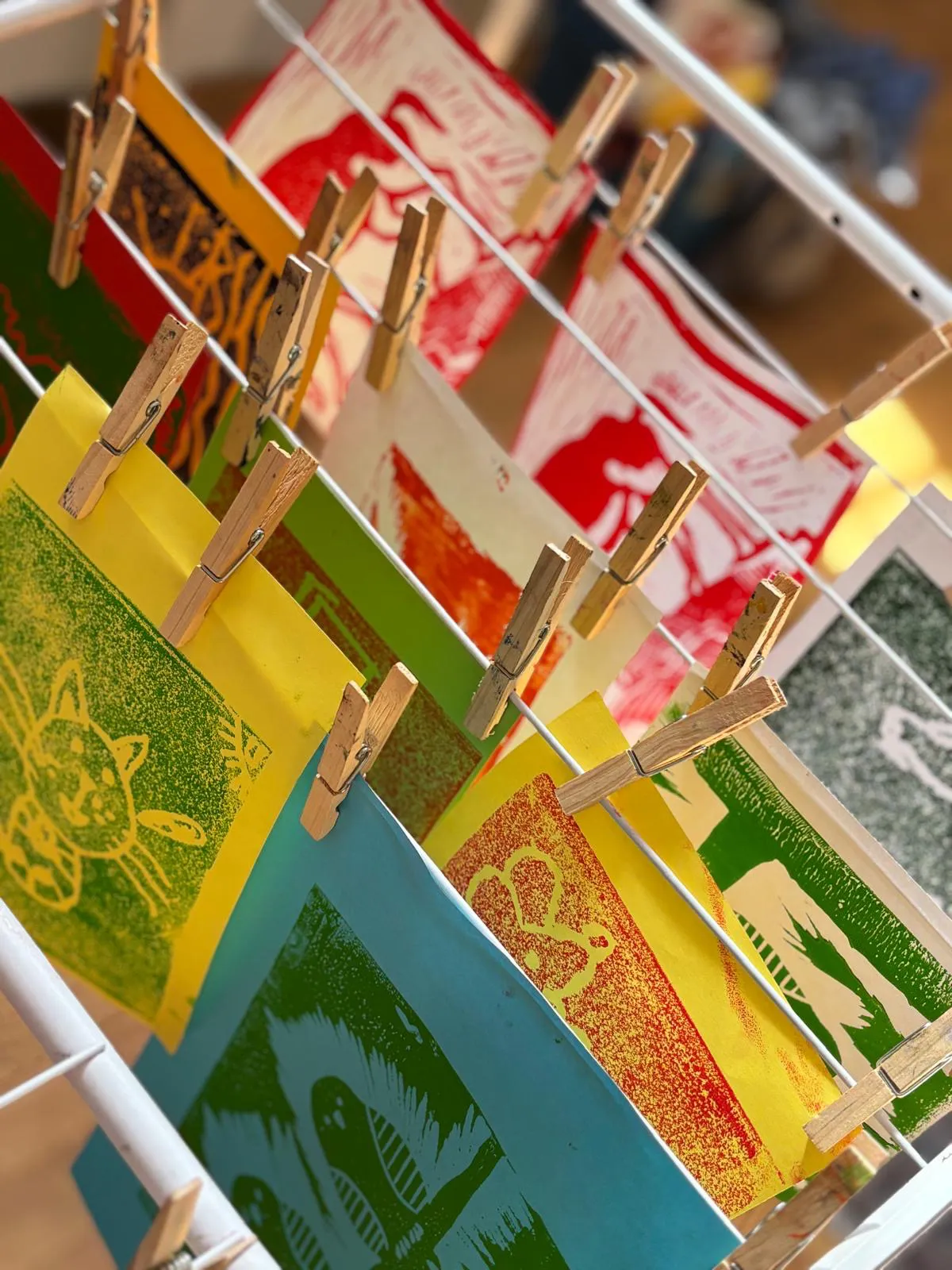 Farbenfrohe Linoldrucke mit verschiedenen Motiven hängen mit Wäscheklammern an einer Leine zum Trocknen.